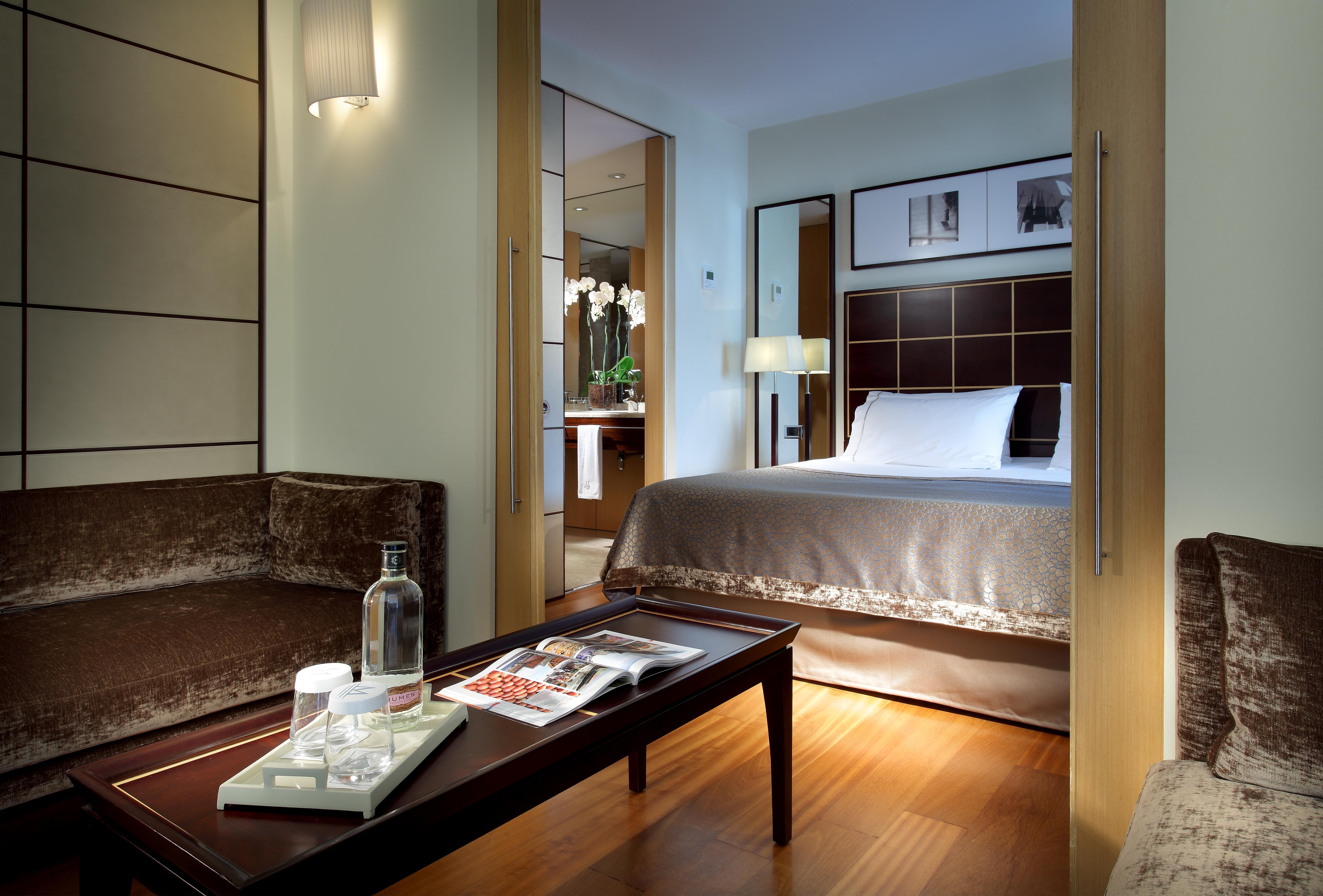 ยูโรสตาร์ แกรนด์ มารีน่า จีเอล โฮเต็ล Hotel บาร์เซโลนา ภายนอก รูปภาพ The image shows a well-decorated hotel room featuring a comfortable bed with a plush headboard, complemented by a subtle color palette. There is a cozy seating area with a brown couch and a coffee table. On the table, there are items like a water bot