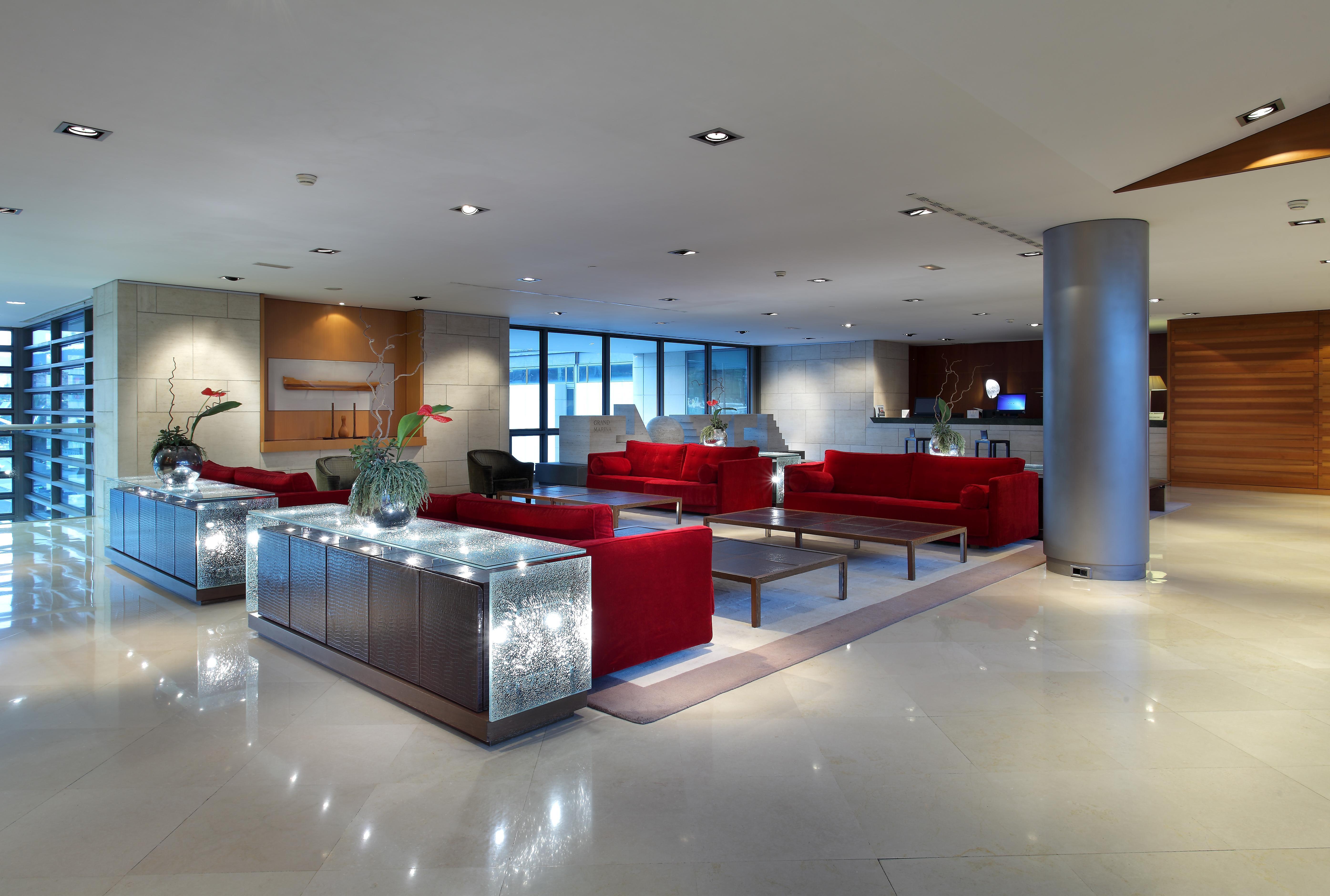 ยูโรสตาร์ แกรนด์ มารีน่า จีเอล โฮเต็ล Hotel บาร์เซโลนา ภายนอก รูปภาพ The photo depicts a modern lobby area, featuring stylish furnishings. There are several red sofas arranged around coffee tables, creating a comfortable seating area. The flooring looks polished and smooth, with a neutral color that complements the fu