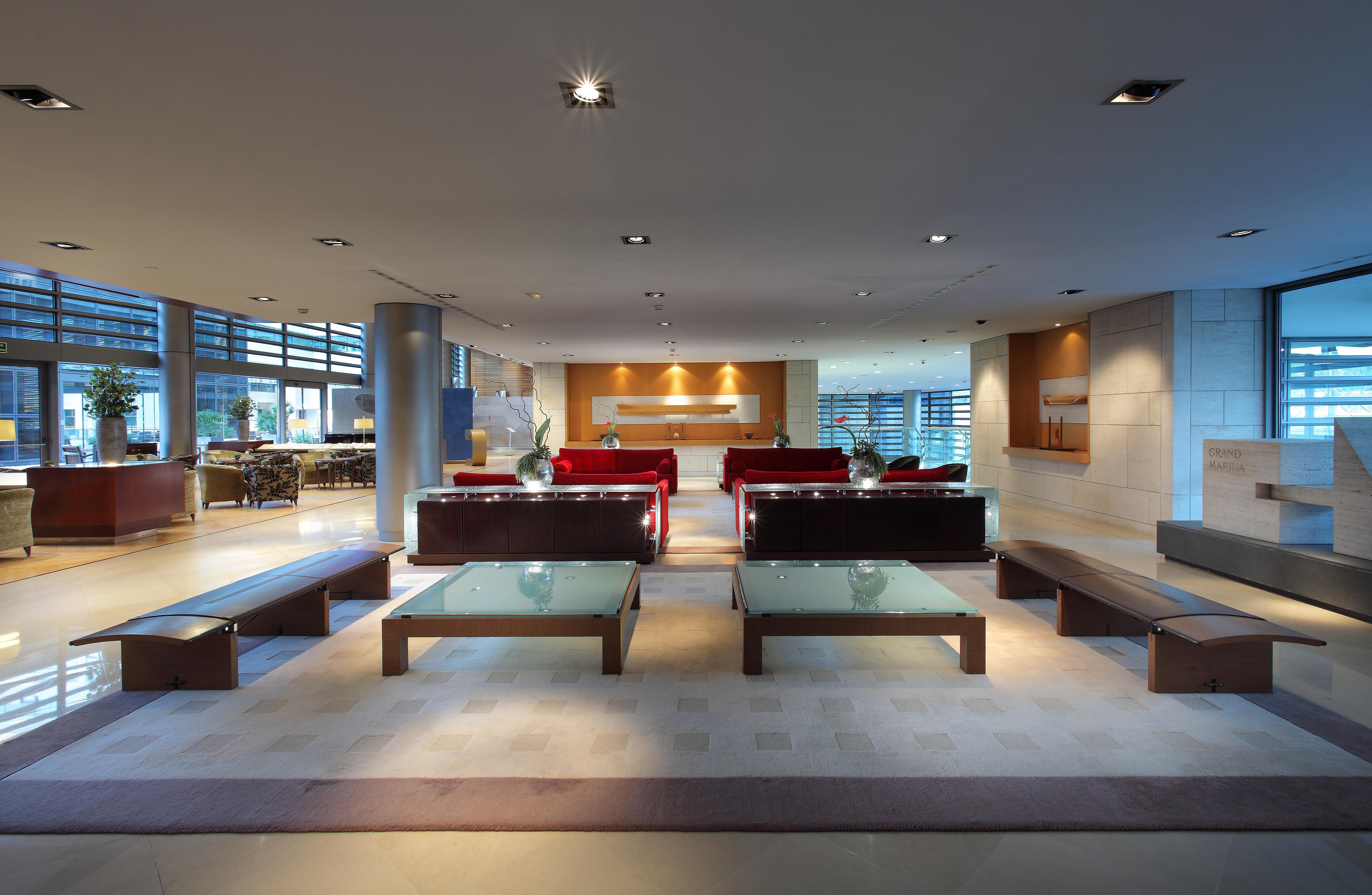 ยูโรสตาร์ แกรนด์ มารีน่า จีเอล โฮเต็ล Hotel บาร์เซโลนา ภายนอก รูปภาพ The photo shows a modern and spacious interior, likely of a lobby or waiting area. It features several red sofas arranged in a conversational layout, complemented by glass-top coffee tables. The lighting is bright and there are large windows, allowin