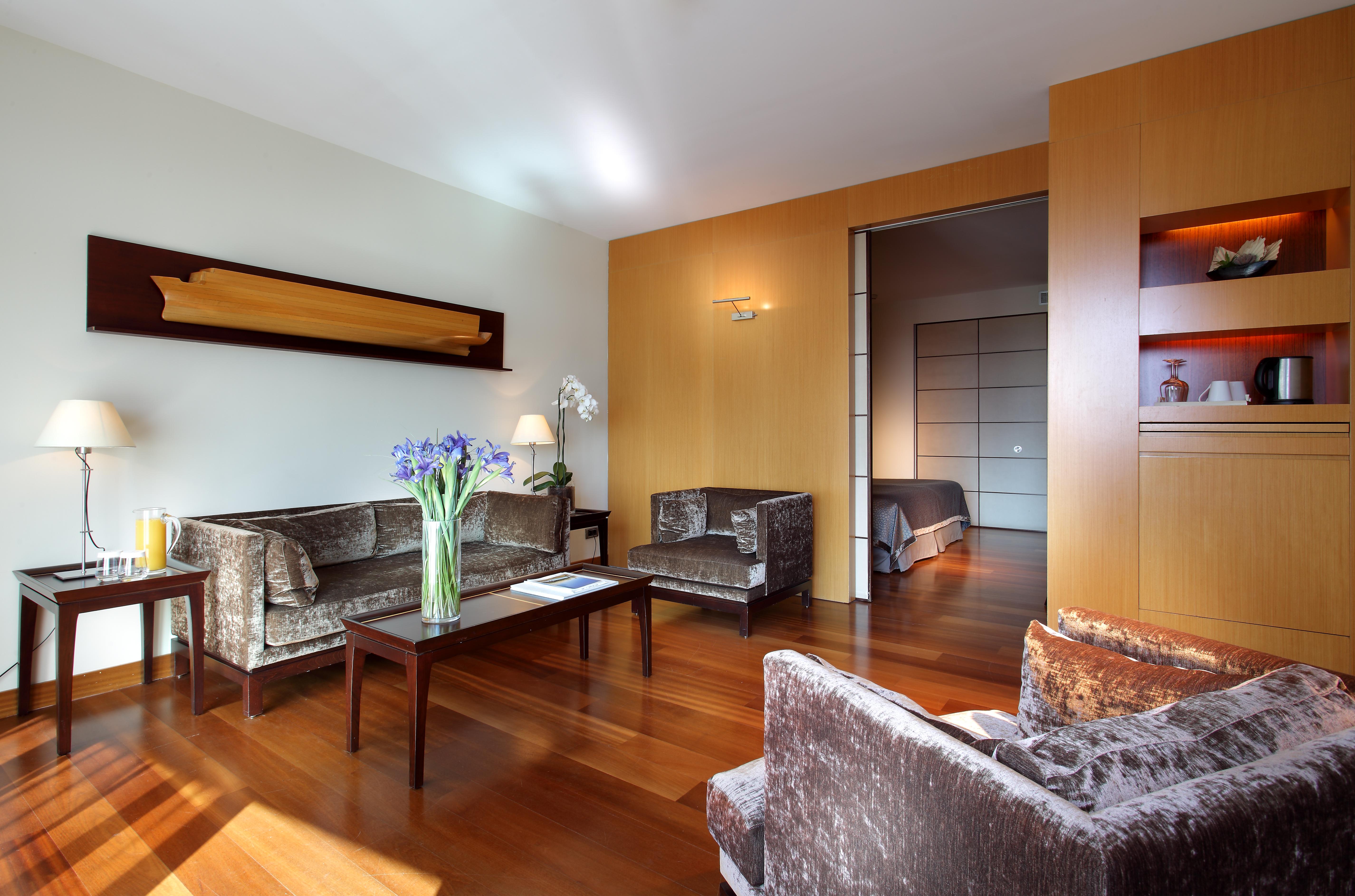 ยูโรสตาร์ แกรนด์ มารีน่า จีเอล โฮเต็ล Hotel บาร์เซโลนา ภายนอก รูปภาพ The photo shows a modern living room with a warm and inviting atmosphere. It features two armchairs and a sofa, all in a plush, dark fabric. A coffee table sits in the center, with a vase of fresh flowers adding a pop of color. The room has hardwood 