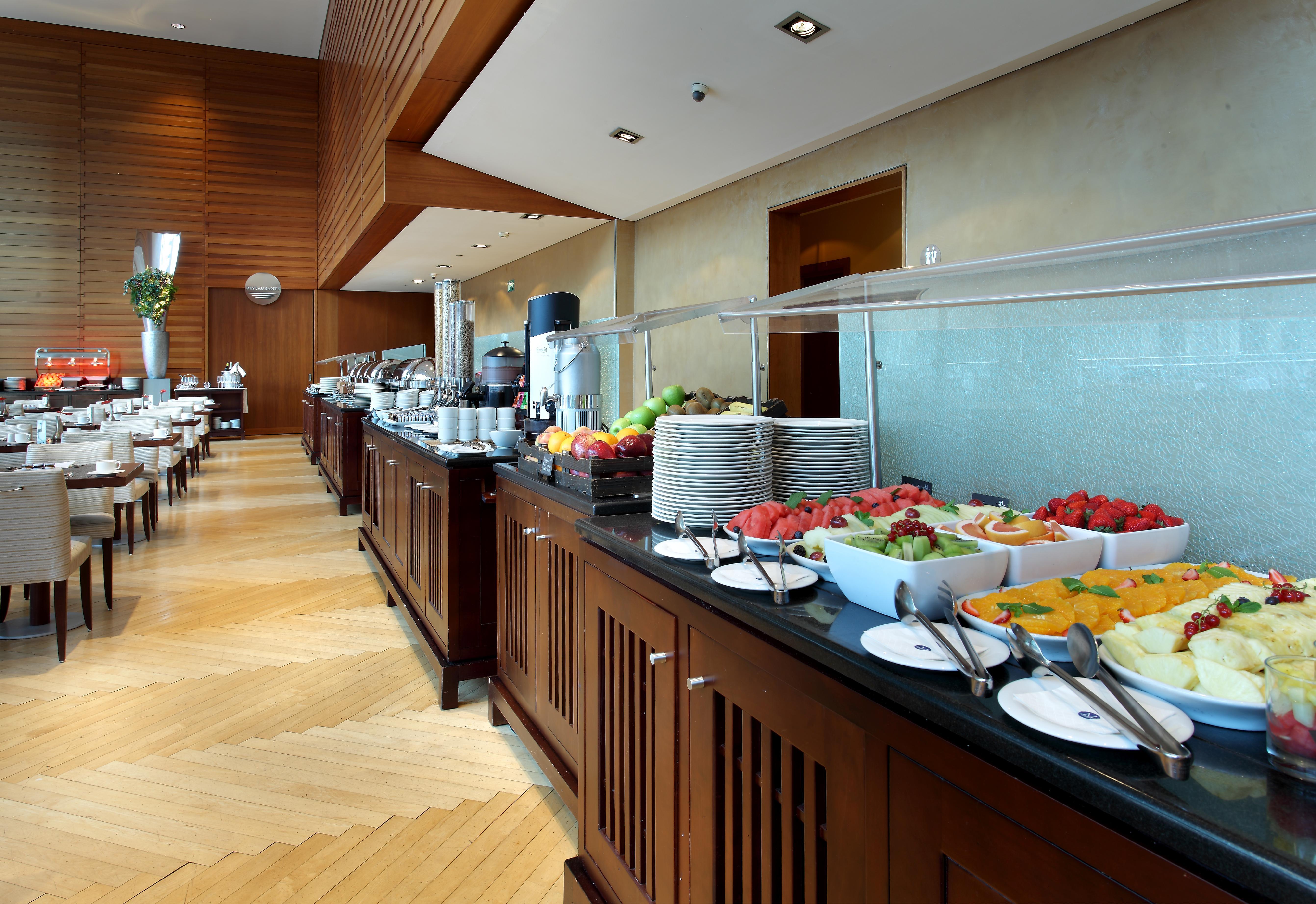ยูโรสตาร์ แกรนด์ มารีน่า จีเอล โฮเต็ล Hotel บาร์เซโลนา ภายนอก รูปภาพ The photo shows a well-organized buffet setup in a modern dining area. There is a long counter made of wood, displaying a variety of food items. Several bowls filled with fresh fruits, such as melons and strawberries, are prominently placed. In the b