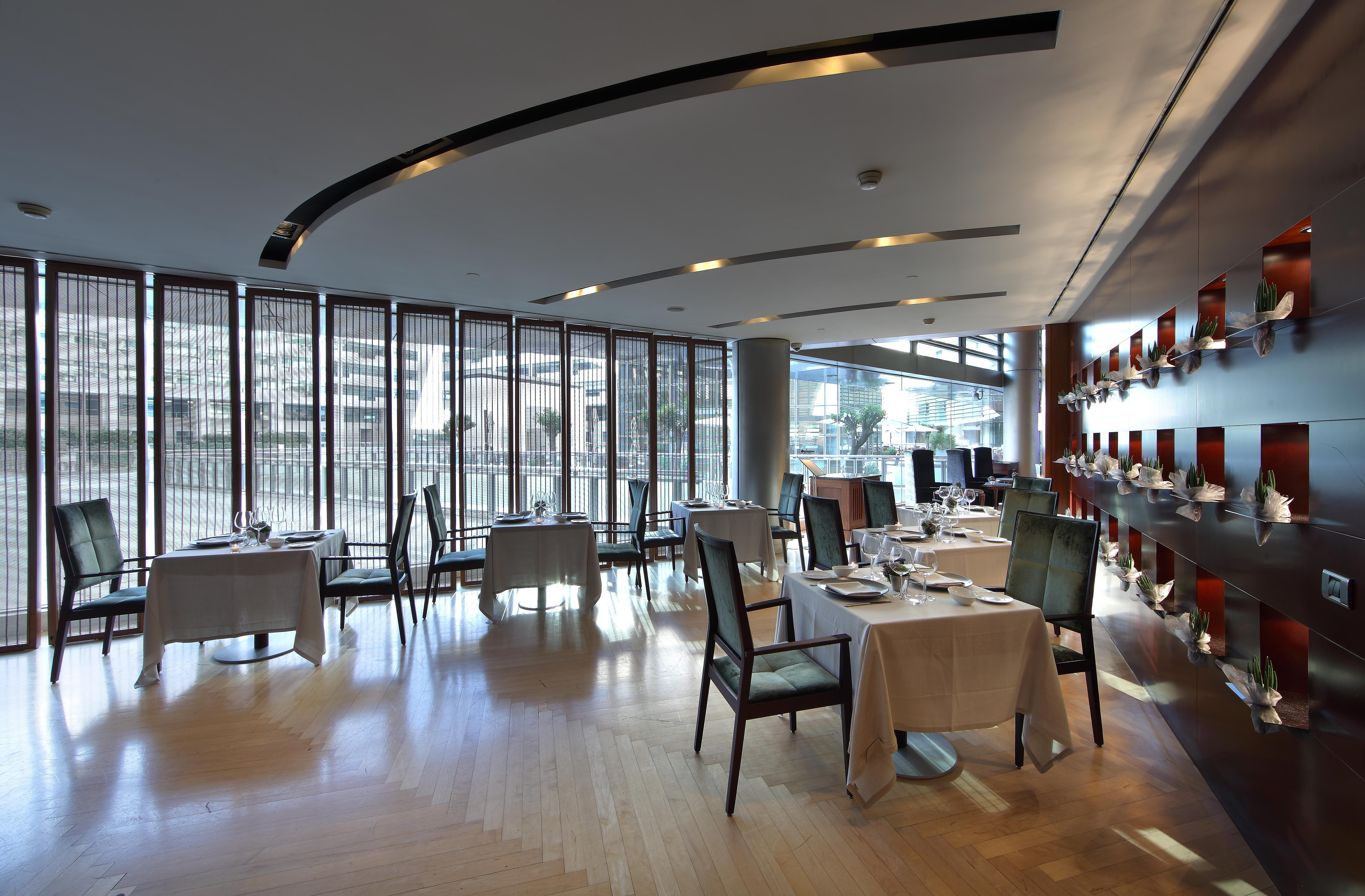 ยูโรสตาร์ แกรนด์ มารีน่า จีเอล โฮเต็ล Hotel บาร์เซโลนา ภายนอก รูปภาพ The photo shows a modern and elegant restaurant interior. There are several dining tables, each covered with tablecloths and set with cutlery. The restaurant features large windows that allow natural light to illuminate the space, creating a warm atm