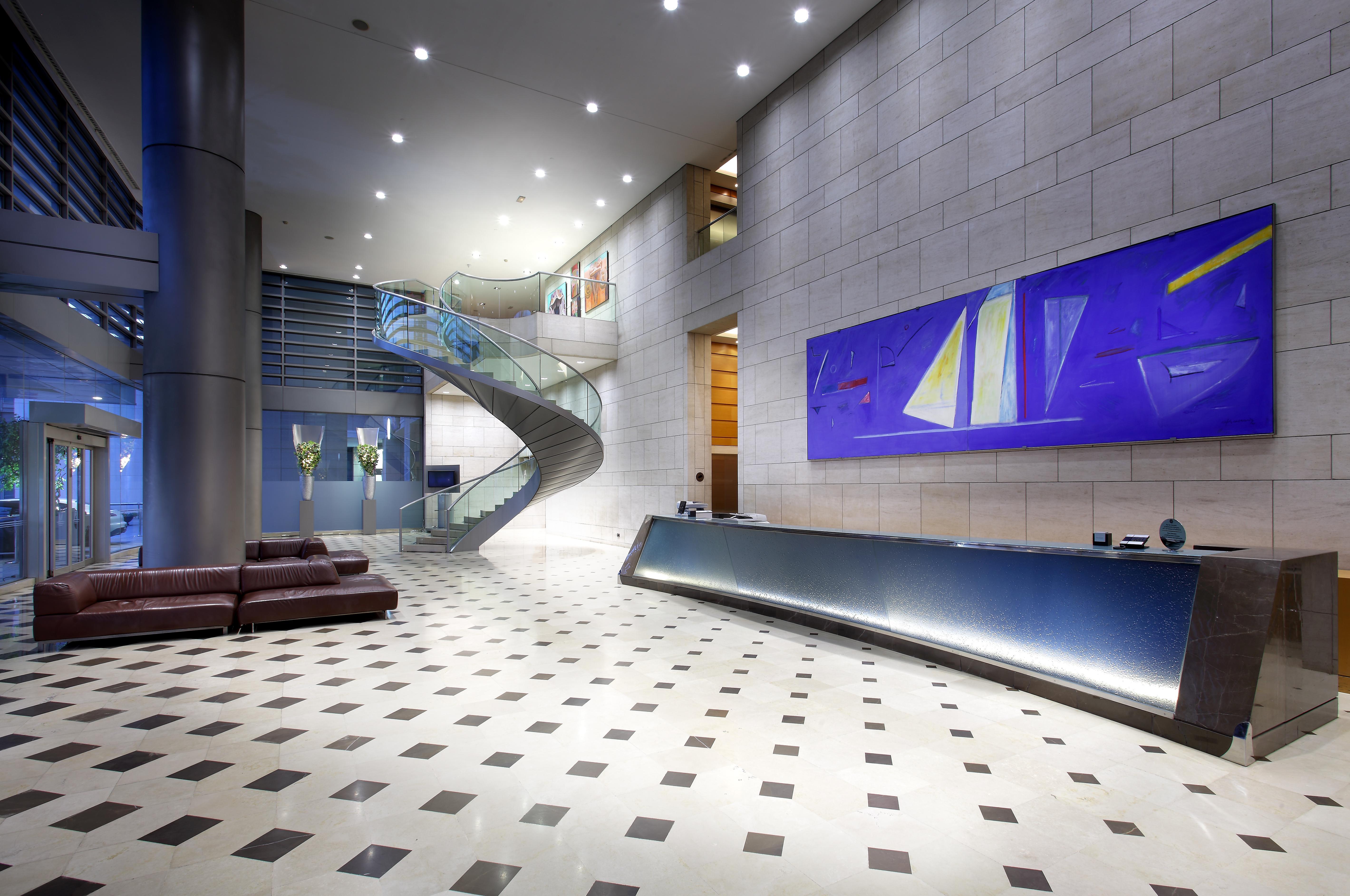 ยูโรสตาร์ แกรนด์ มารีน่า จีเอล โฮเต็ล Hotel บาร์เซโลนา ภายนอก รูปภาพ The photo shows a modern lobby or reception area. There is a sleek reception desk along one wall, featuring a polished surface. To the left, a spacious staircase with a glass guardrail leading to an upper level can be seen, framed by walls decorated 