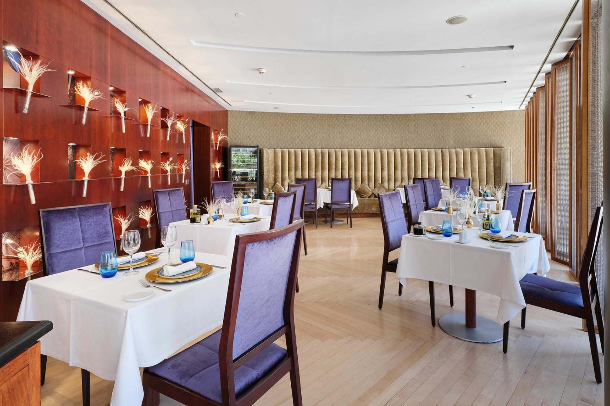 ยูโรสตาร์ แกรนด์ มารีน่า จีเอล โฮเต็ล Hotel บาร์เซโลนา ภายนอก รูปภาพ The photo shows an elegant dining room in a restaurant. There are several tables set with white tablecloths, each adorned with plates, glasses, and decorative items. The chairs have a purple upholstery, adding a touch of color to the space. 

The wal